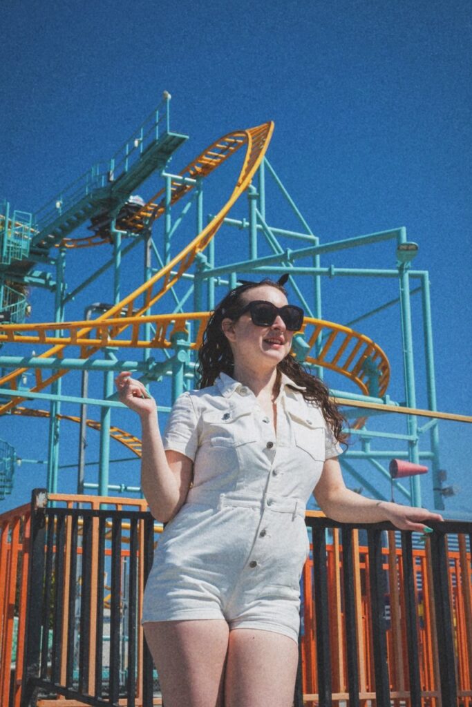 delphine a brunette woman in a white jumpsuit in front of the roller coaster at the santa cruz boardwalk