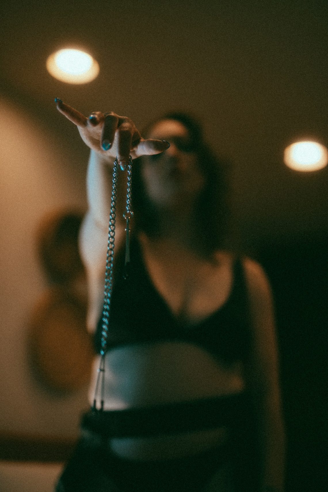 Delphine is wearing a black bra and holding up nipple clamps to the camera.