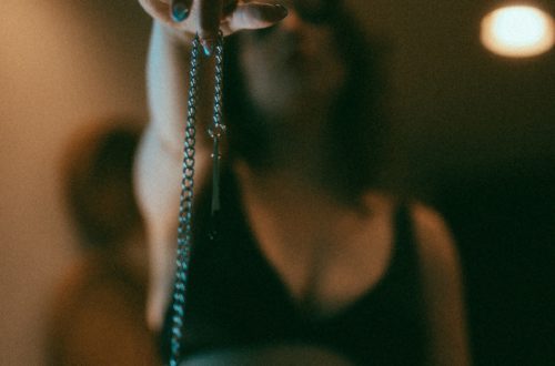 Delphine is wearing a black bra and holding up nipple clamps to the camera.