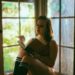 Delphine is sitting in a bay window reading a book. She is wearing lingerie and knee socks.