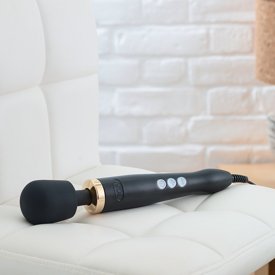 Photo of a black vibrator with a gold accent on a white couch. 