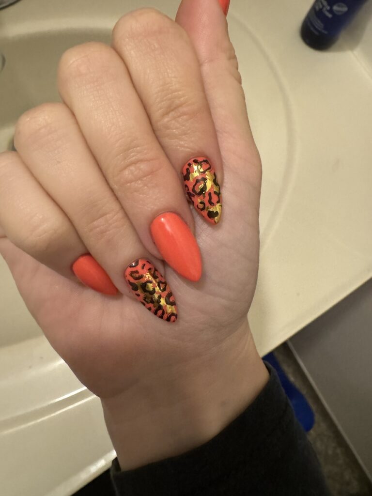 Close up of Delphine's nails. They are orange with gold and black leopard print.